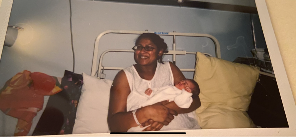 A photograph of Sarah Guerra (the author) smiling with her daughter Kaela, who is one day old, in a hospital bed.