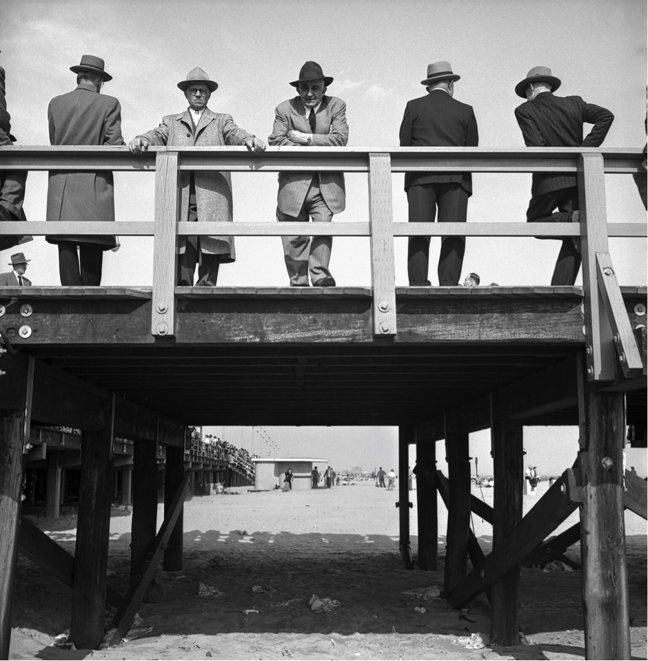 Black and white image of men standing on a small pier wearing coats and hats