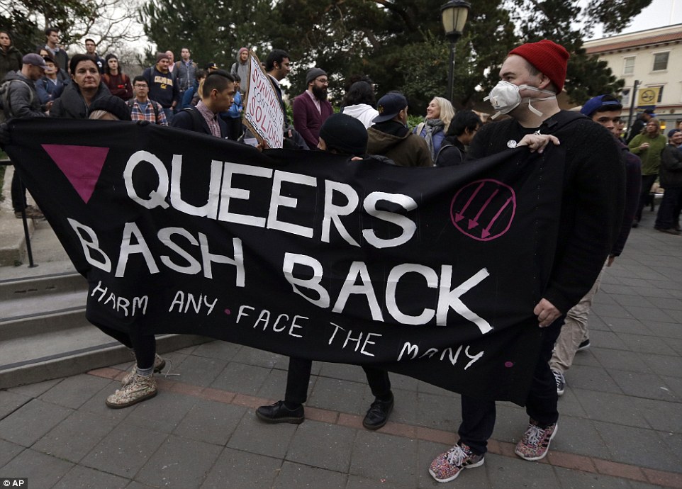 Image via AP: Two protesters wearing black carry a black banner emblazoned with 'Queers Bash Back: Bash Any Face the Many' 