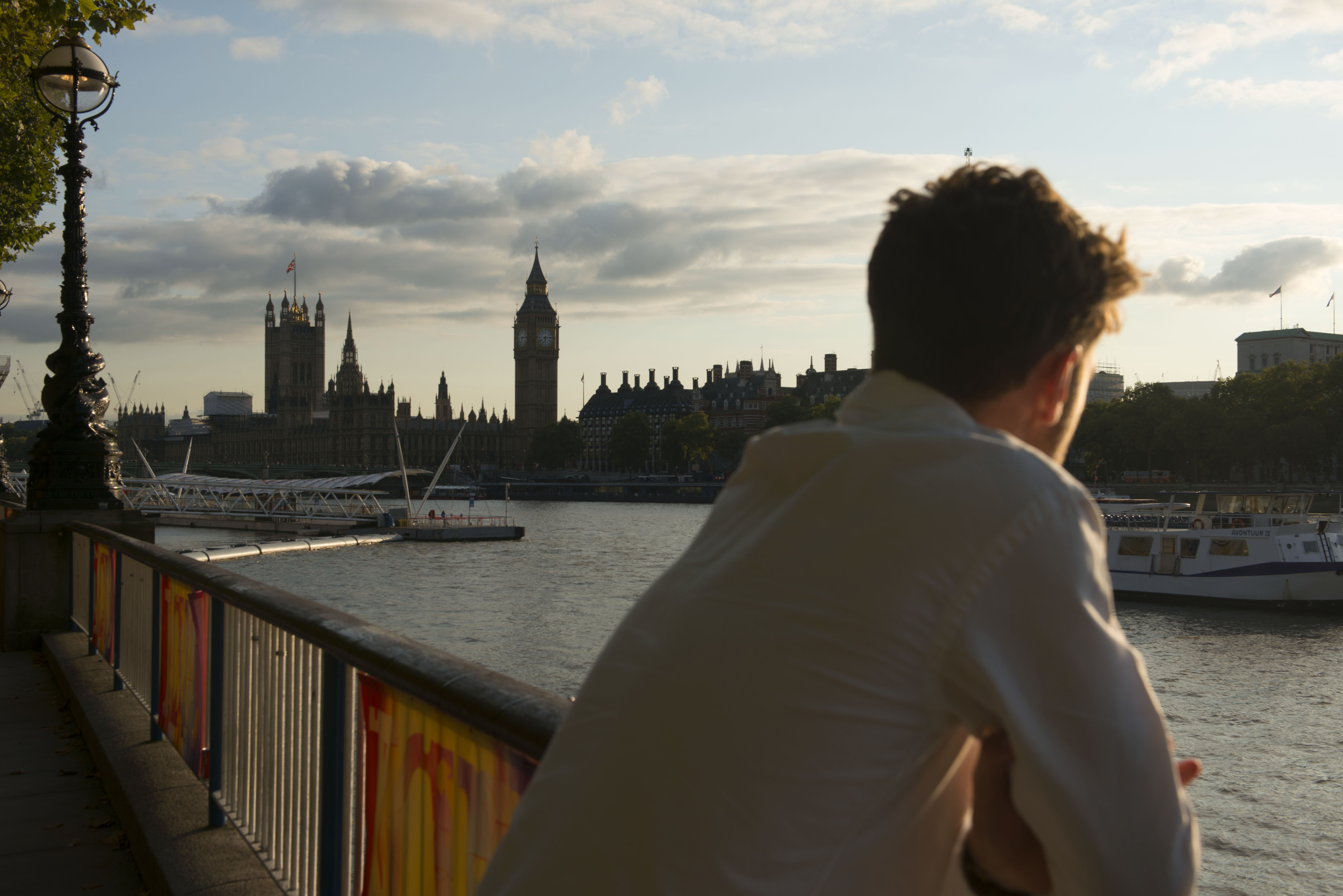 A close up photograph of a man's back as he looks at the British Houses of Parliament across the River Thames.
