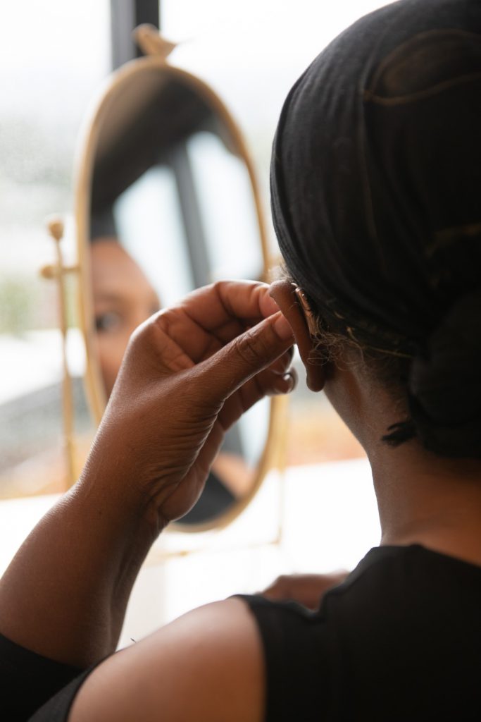 A woman putting on a hearing aid in front of her desk mirror