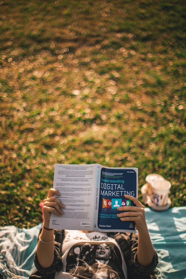 person lying on grass reading book, which is titled 'digital marketing'