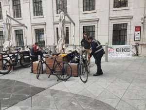 Two photographs showing a bike mechanic looking at a bicycle in the courtyard of Bush House.
