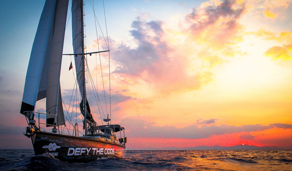 A photo of a McGregor sailboat on the ocean with a colourful sunset