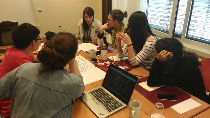 Students sit round a table in a small room concentrating on a problem.