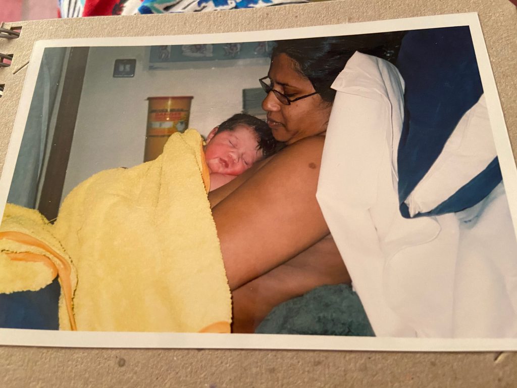 A photograph of Sarah Guerra (the author) in side profile with daughter Lyra, just born, covered with a yellow blanket.