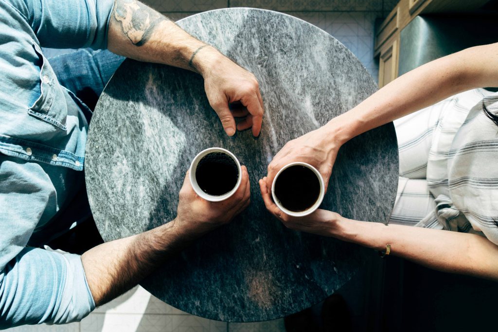 Ariel shot of a man and a woman holding two cups of coffee on a round coffee table.