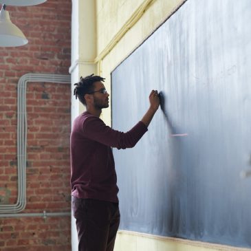 Image of man writing to chalkboard. Click here to read the blog