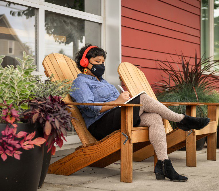 woman with facemask and headphones sitting on chair