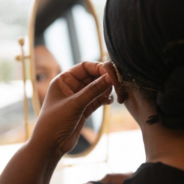 A woman putting on a hearing aid in front of her desk mirror
