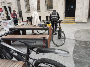 Two photographs showing a bike mechanic looking at a bicycle in the courtyard of Bush House.